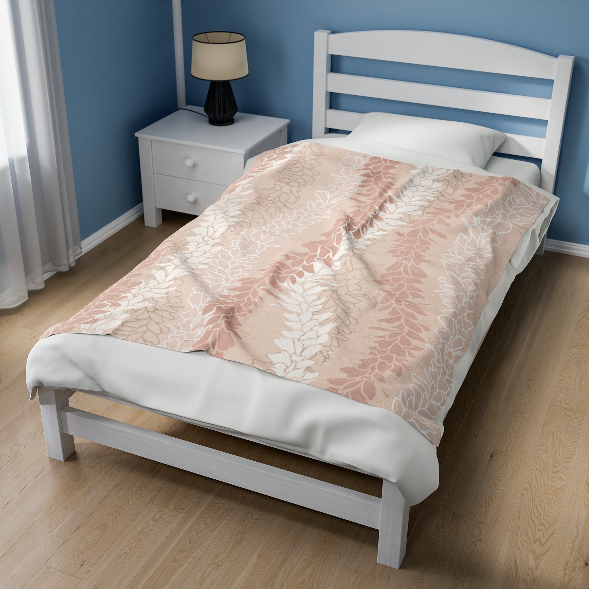 Peach blanket with Hawaiian flower lei design of cream, pink and gray flower lei silhouettes and outlines. Blanket is laying on a single bed with white bedding and white wood frame along side a white nightstand and neutral color lamp.