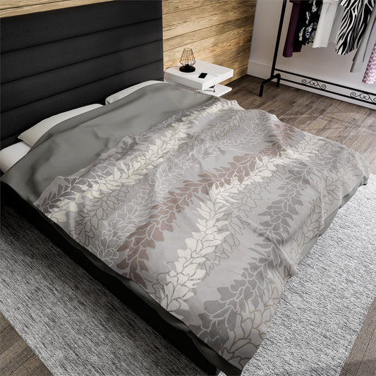 Delicate hanging strands of cream, brown and gray awapuhi ginger flower lei on a light gray velveteen blanket throw draped on a queen size bed in classic modern bedroom in neutral colors.