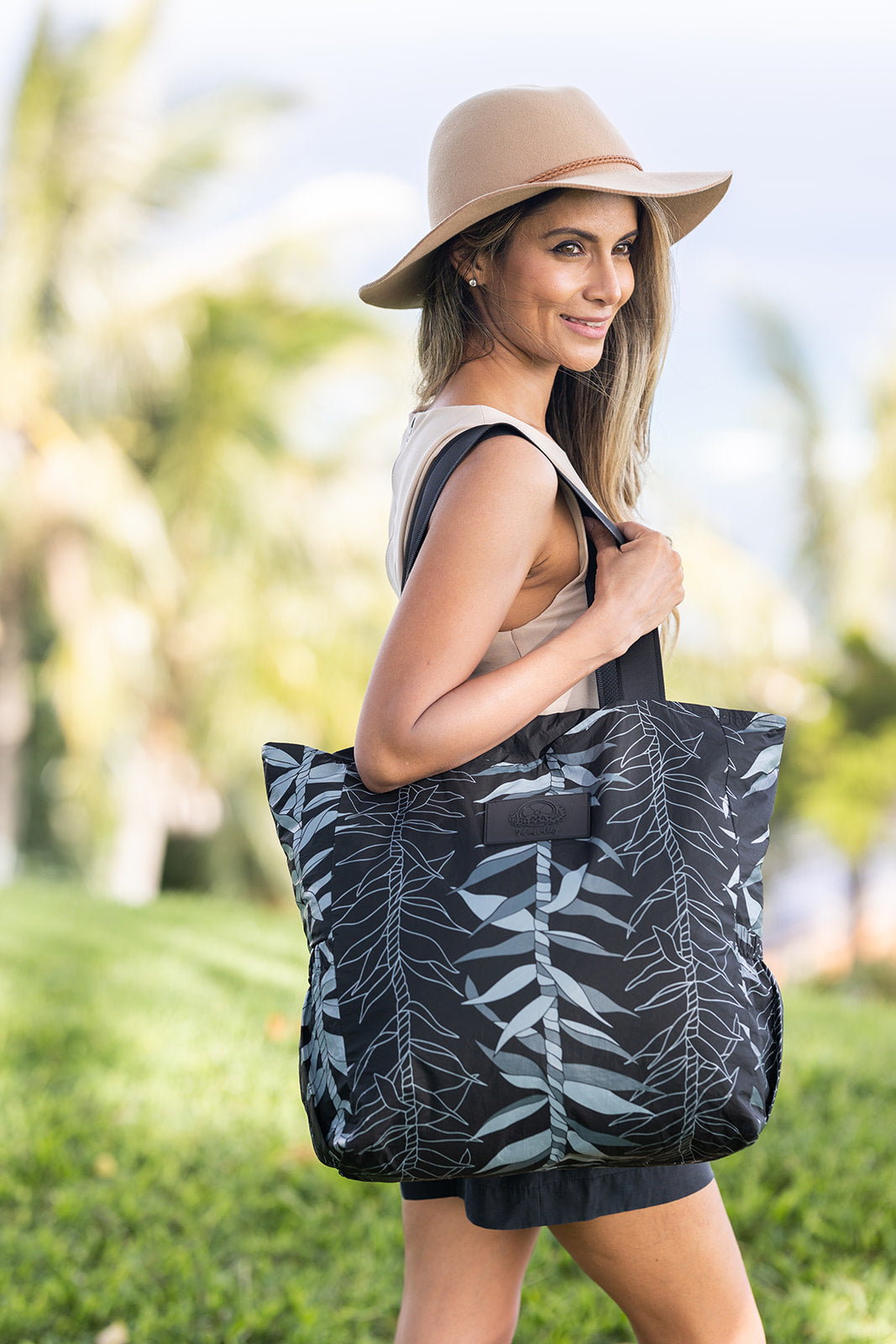 Model holding black ti leaf tyvek tote bag in the Hawaii park on a summer day.  