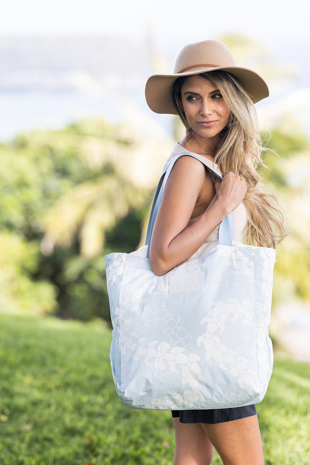 Blue and White puakenikeni flower lei design on tyvek tote held by beautiful model on a sunny day in Hawaii park. 