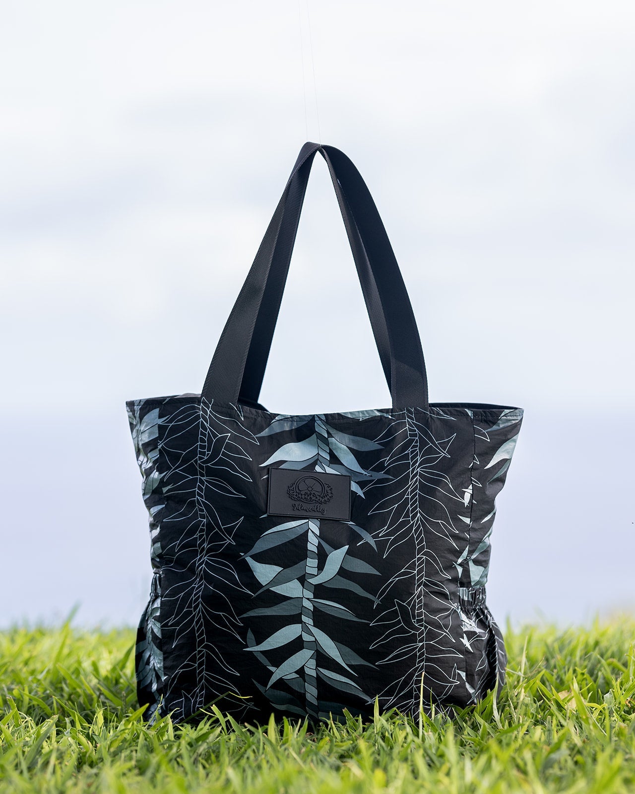 Neutral Black and gray Ti leaf tyvek tote bag in the grass.