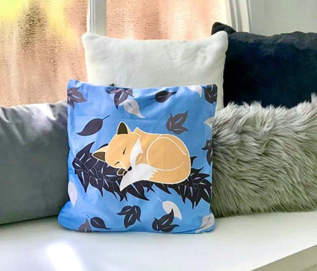 blue and gray faux suède pillowcase with sleeping fox on maile lei on window sill with other gray, dark blue and white pillows