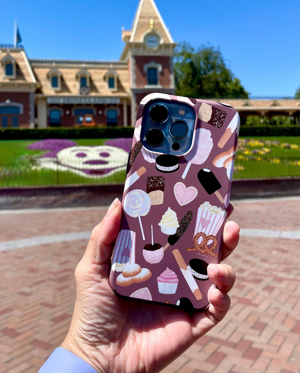 Cute happiest snacks dual layer iphone tough case in front of Mickey grass entry at Disneyland Park.  