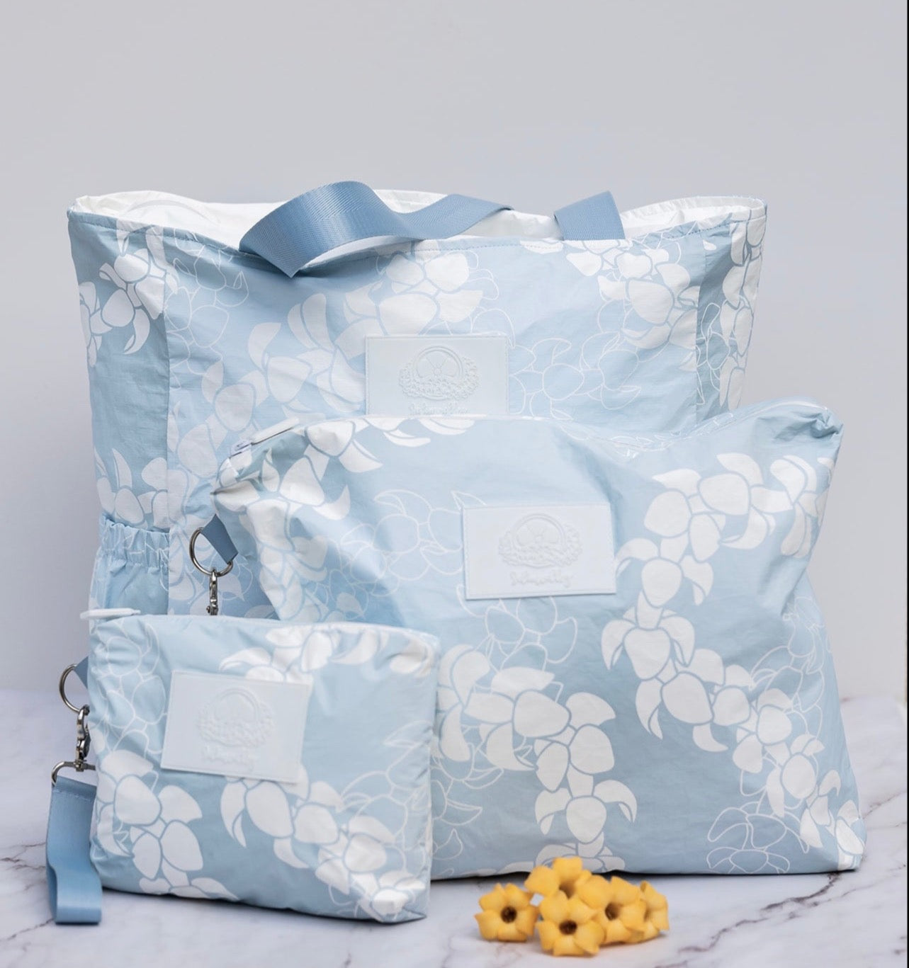 Light blue and white Puakenikeni flower lei tyvek tote and matching small and large accessory pouches.