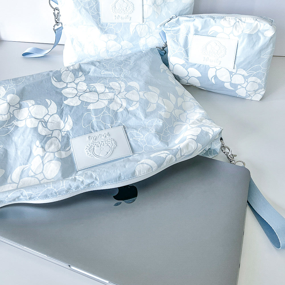 Small, medium and large Puakenikeni lei tyvek accessory pouches with large pouch opened holding MacBook laptop.  