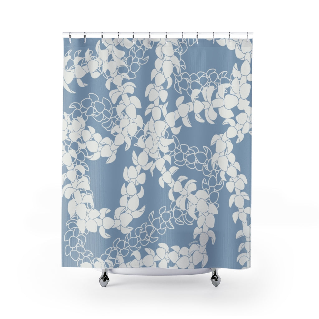 A blue shower curtain with white curvilinear puakenikeni flower lei in a crossing floral pattern, displayed in a bathroom setting.