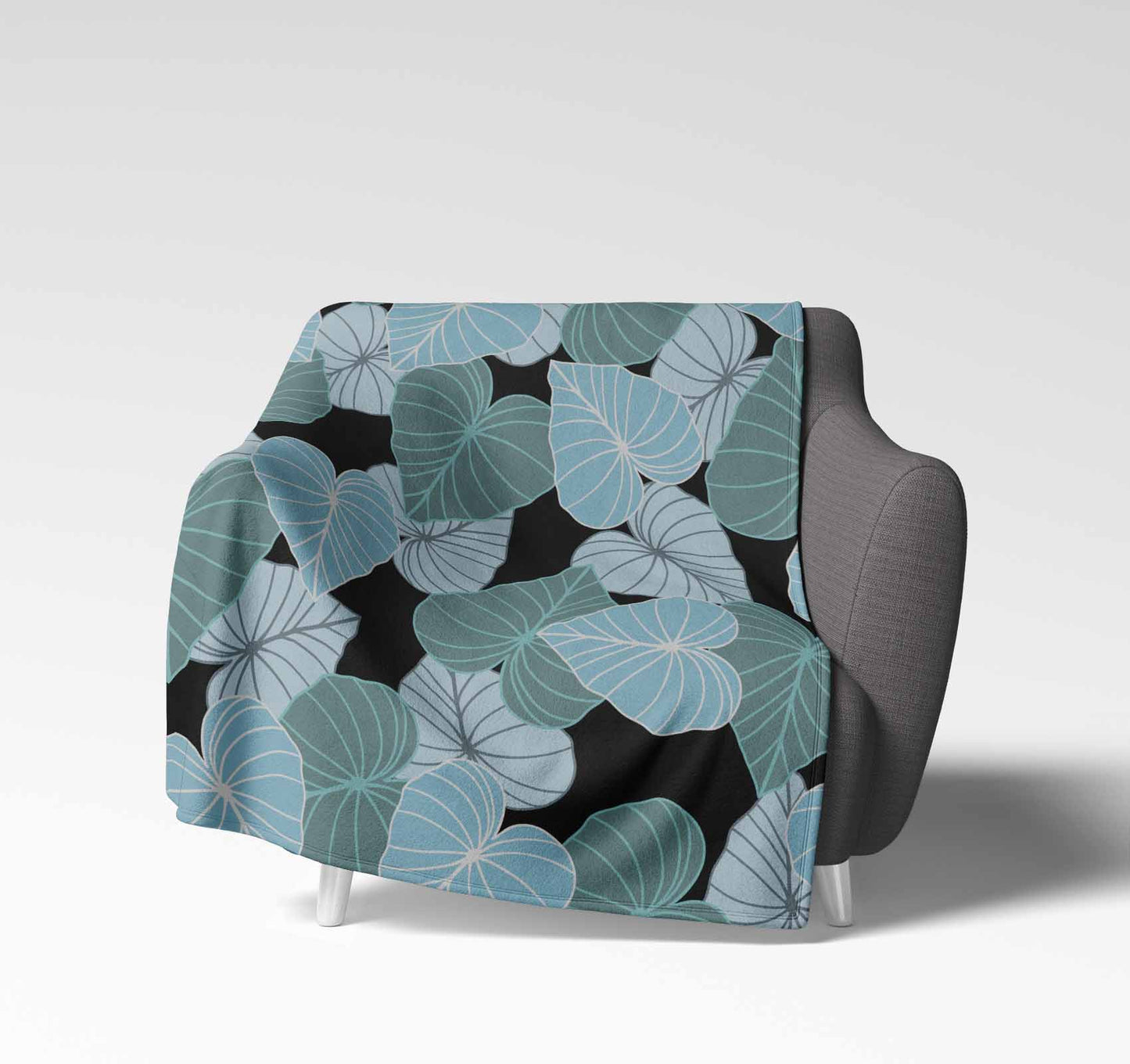 Soft velveteen blanket with a design displaying layers of Kalo leaves of different shades of blue green in an all-over-print pattern on a black background.