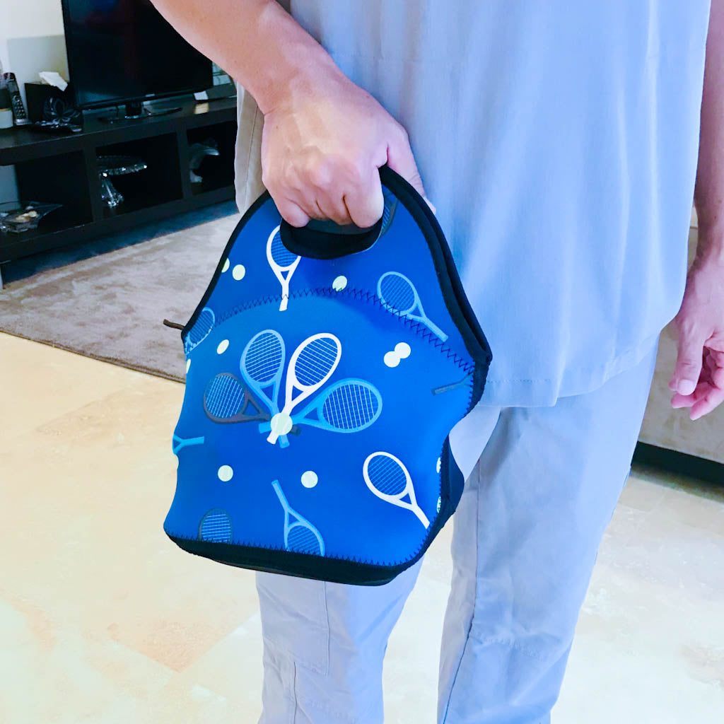 Male wearing gray scrubs holding blue neoprene lunch bag with tennis racket design.