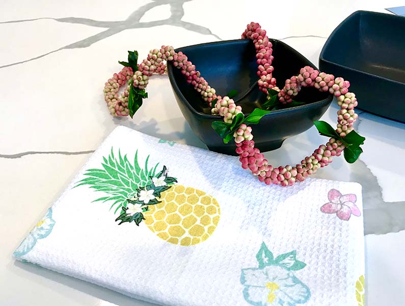 cute pineapple wearing flower crown haku lei, hibiscus and plumeria dishtowel on kitchen counter