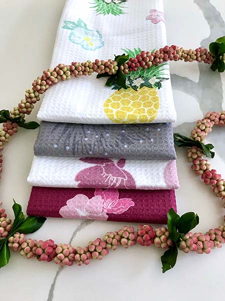 set of cute island style dishtowels featuring pineapple, hibiscus and plumeria design encircled with a lei